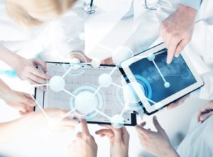 A group of doctors looking over iPad screens displaying holographic connections