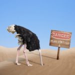 Ostrich with it's head in the sand next to a "danger" sign