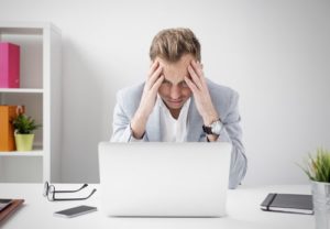 Man sitting at desk looking at laptop in frustration