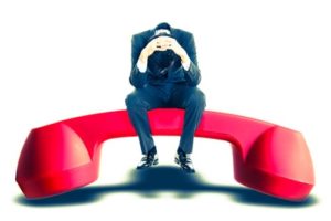 Person wearing suit sitting in frustration on a giant red telephone